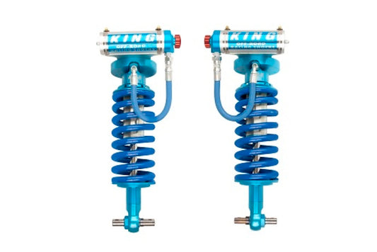 Displayed against a white background are a pair of King Shocks 2007+ Chevrolet Avalanche 1500 Front 2.5 Dia Remote Res Coilovers with Adjusters, featuring coiled springs, remote reservoirs, hoses, and the "King" branding. These blue off-road shock absorbers are perfect for enhancing the rugged performance of vehicles like the Chevrolet Avalanche.