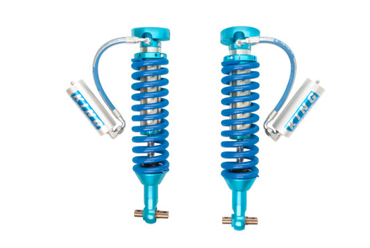 King Shocks 2017+ Chevrolet Colorado ZR2 Front 2.5 Dia Remote Reservoir Coilovers, featuring blue springs and a polished metallic finish. Arranged side by side on a white background, they proudly exhibit the "King Shocks" brand logo, akin to the high-end suspension systems used in vehicles like the Chevrolet Colorado ZR2.