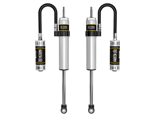 Displayed are a pair of silver ICON 11-19 GM HD 0-2in Front 2.5 Series Shocks VS RR with Upper Control Arm, each featuring a black reservoir tube attached at the top. These vehicle-specific shocks are designed for off-road performance and showcase ICON’s commitment to high-performance suspension components and advanced compression damping control valve technology.