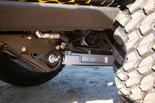 A close-up of the ICON 21-23 Ford Bronco Rear 2.5in VS RR Coilover Kit Heavy Rate Spring showcases adjustable coilovers and rugged tire tread on a dirt surface, emphasizing the ICON suspension system's durability and ability to handle rough terrain.
