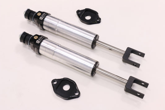Two ICON 11-16 GM HD 6-8in Front 2.5 Series Shocks, manufactured by ICON, are displayed on a white background. These silver shocks come with black mounts and include visible adjustment knobs as well as multiple mounting holes for enhanced off-road performance. Designed to be rebuildable, they ensure lasting durability and come with an upper control arm for easy installation.