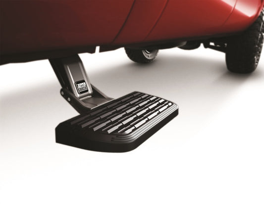 A close-up of an AMP Research 1999-2013 Chevrolet Silverado All Beds BedStep2, extending from beneath a red truck. The black retractable step features a textured surface for enhanced grip, contrasting with the smooth and light-colored surrounding area.