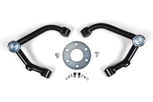 A BDS Upper Control Arm Kit for Chevy Silverado and GMC Sierra 1500 (07-18), featuring two black metal upper control arms, a circular metal plate with multiple holes, and various bolts, nuts, and washers, is spread out on a white background.