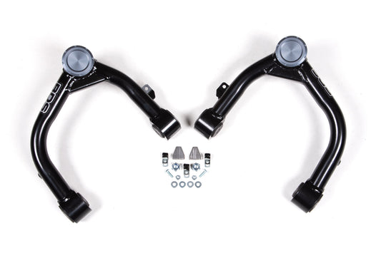 Two black upper control arms with metallic caps on one end, presented symmetrically. Between them are several small components, including bolts, nuts, washers, and brackets for a BDS Upper Control Arm Kit for Chevy Silverado and GMC Sierra 1500 (19-23) with Adaptive Ride Quality—all arranged neatly on a white background.