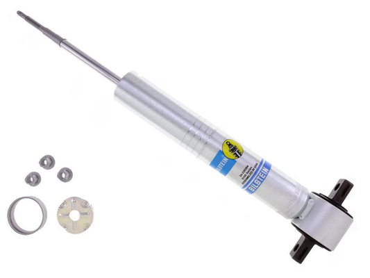 Image of a Bilstein B8 5100 Series 19-24 GM 1500 AT4/Trail Boss Front Shock Absorber by Bilstein Shocks with accessories. The metallic shock absorber, featuring a clear label, is displayed at an angle. Accessories include several washers, a ring, and a mounting bracket placed beside the monotube design shock absorber.