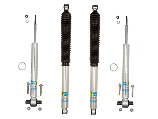 Four LTW Motorsports shock absorbers from the 15-20 Ford F-150 2WD Leveling Kit with Bilstein 5100 Shocks are arranged vertically on a white background. Two feature black accordion-style dust boots, designed to enhance off-road performance, while the others lack this feature. Bolts and washers are placed next to them, completing this setup ideal for a Bilstein leveling kit.