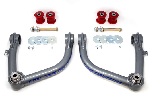 Two 19-24 GM 1500 Upper Control Arms by TOTAL CHAOS, featuring gray suspension arms, are centered with red bushings, bolts, washers, and spacers symmetrically arranged on a white background to showcase the precision of lift kits for enhanced performance.