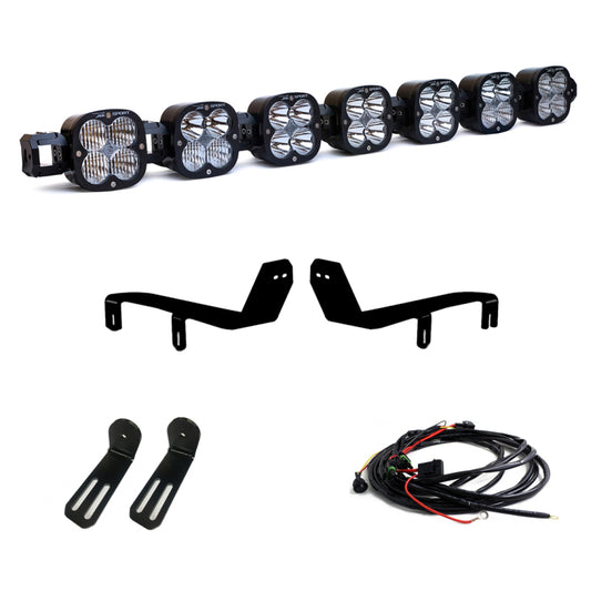 The Baja Designs 17-19 7 XL Linkable LED Light Kit For Ford Super Duty includes a set of seven off-road LED driving lights, complete with a wiring harness and mounting hardware. Designed specifically for the Ford Super Duty, this kit features two L-shaped brackets, smaller mounting plates, and installation cables. The LED lights are arranged in a sleek black row.