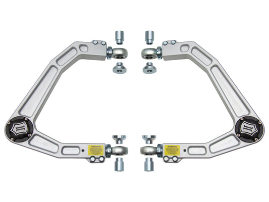 A set of ICON 2019+ GM 1500 billet upper control arms with Delta Joints and all necessary hardware, including bushings, are arranged symmetrically on a white background. The arms feature a sleek silver design with corrosion-resistant properties and prominently display the ICON brand logos near the corners.