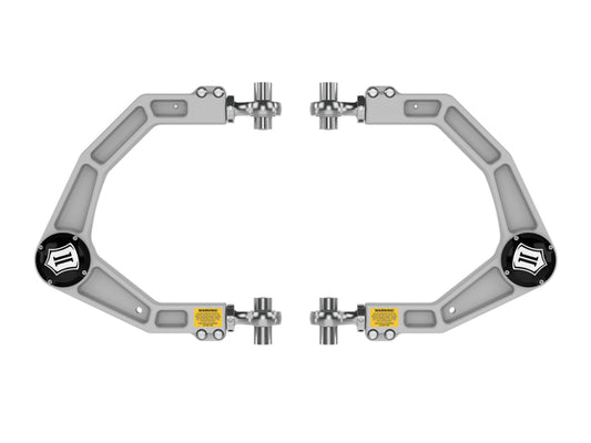 A set of geometric brackets made of metallic material, featuring black circular centers embellished with logos. These brackets highlight the Delta Joint PRO by ICON for advanced suspension articulation, incorporating pivotable joints and labeled caution stickers against a white backdrop. They are part of the Icon Ford F-150 Raptor Billet Upper Control ARM w/ Delta Joint Pro Kit.