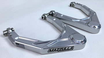 A pair of MAZZULLA OFFROAD 2019+ CHEVY/GMC 1500 LONG TRAVEL billet aluminum upper control arms are shown against a white background. They are metallic silver with prominent branding and detailed machining, designed for high-performance automotive applications, particularly suitable for offroad vehicles equipped with a long travel kit.