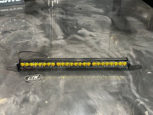 A slim LED light bar with multiple yellow lights sits on a shiny surface. The light bar features black brackets compatible with the 22-25 Chevy Silverado 1500 grille. A power cable is attached, and an "LTW Motorsports" logo is nearby.